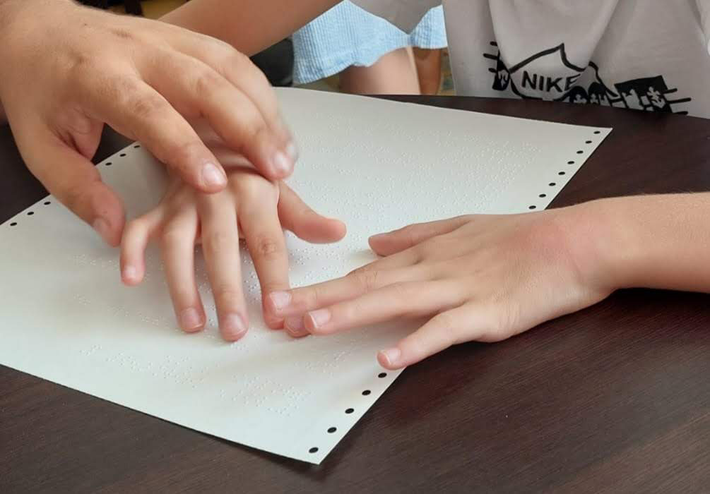 Reading and guiding a child with a worksheet printed in braille.